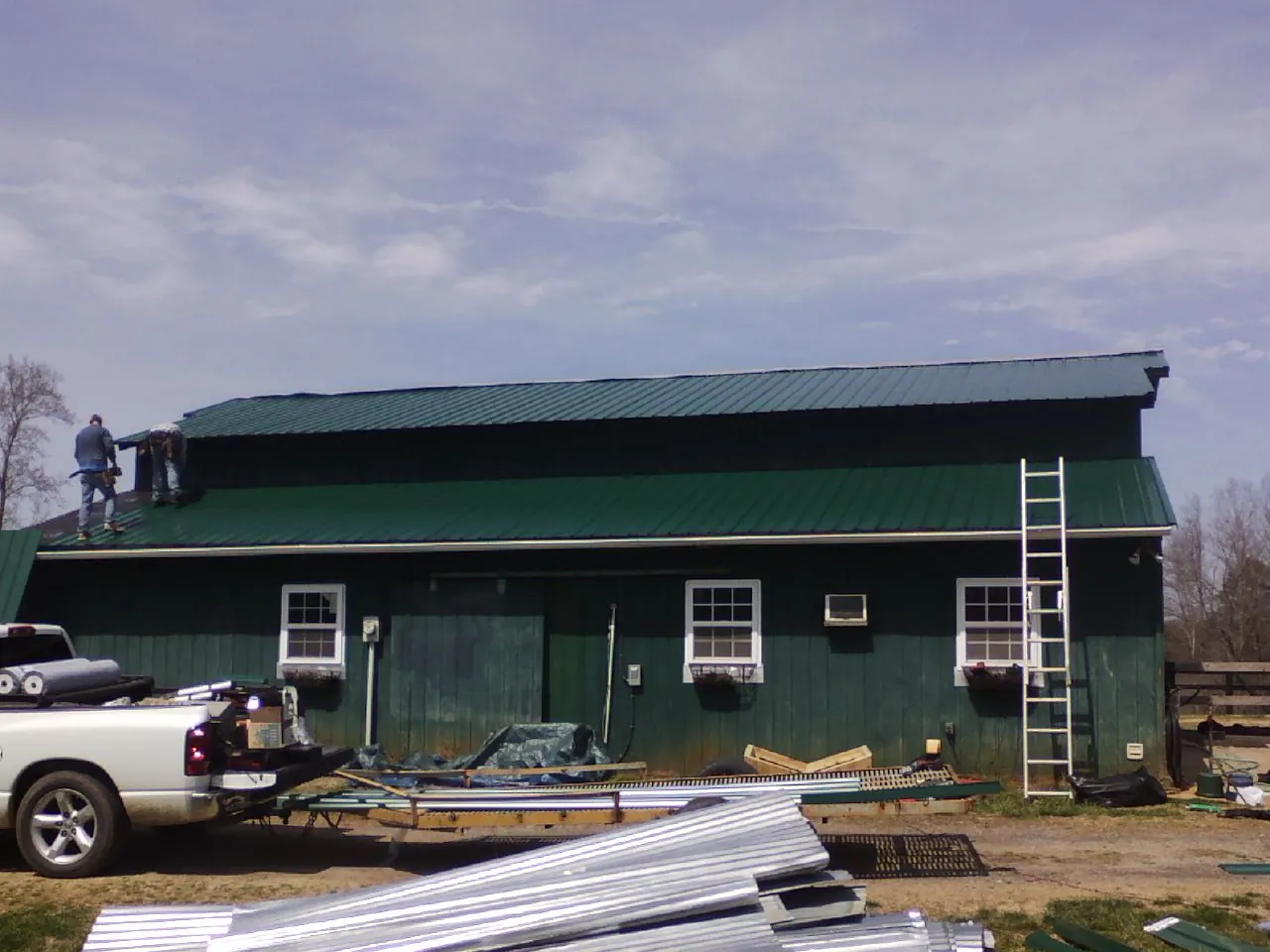 Crew installing green metal roofing on a large green barn in Elizabeth